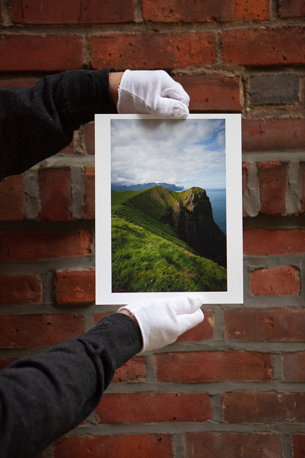 Hands with white gloves holds archival pigment print of a beautiful landscape against a brick wall background